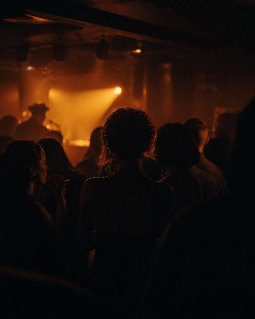A crowd lit by warm stage haze in a small live-music room